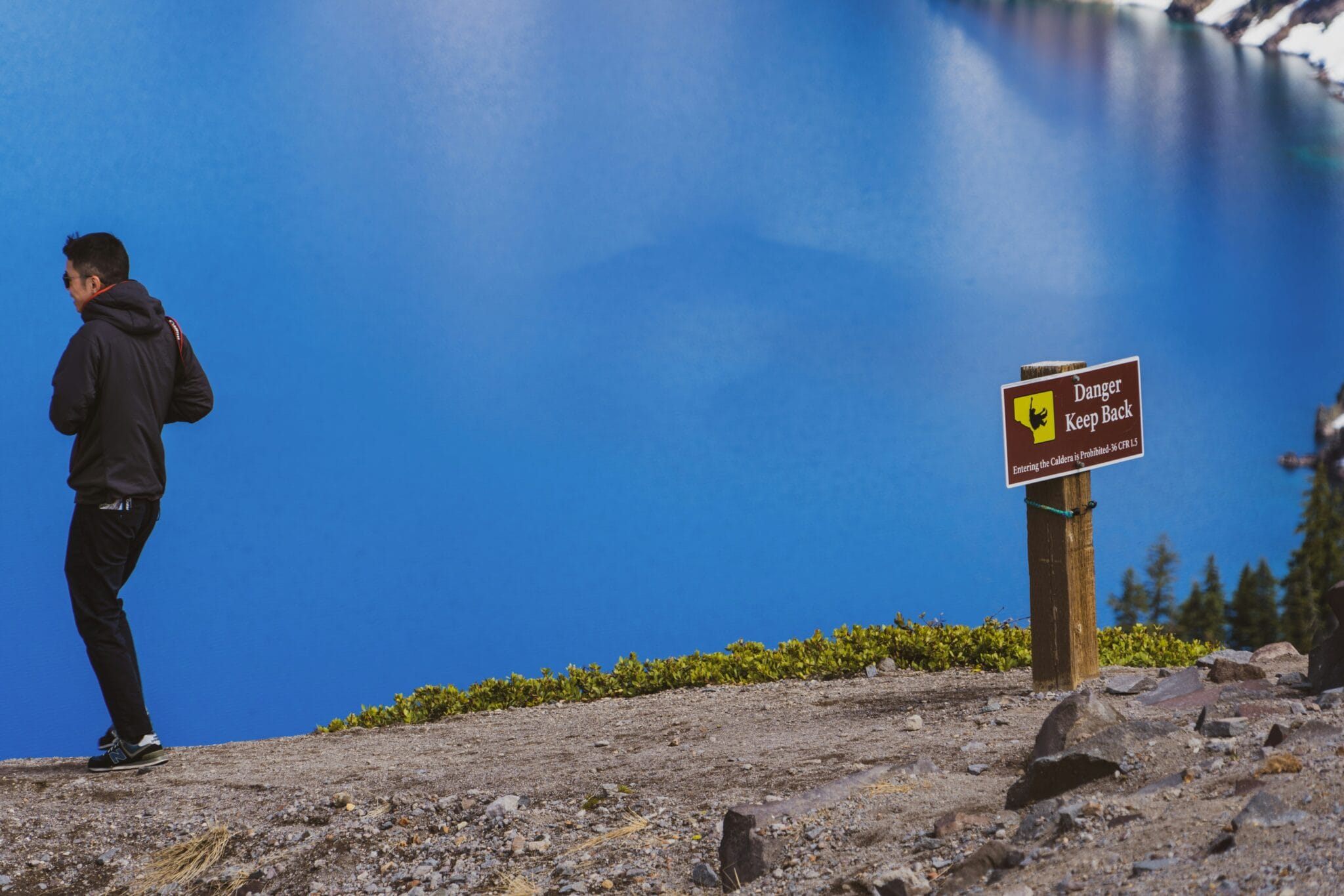 man walking away from danger keep away signage by the blue lake